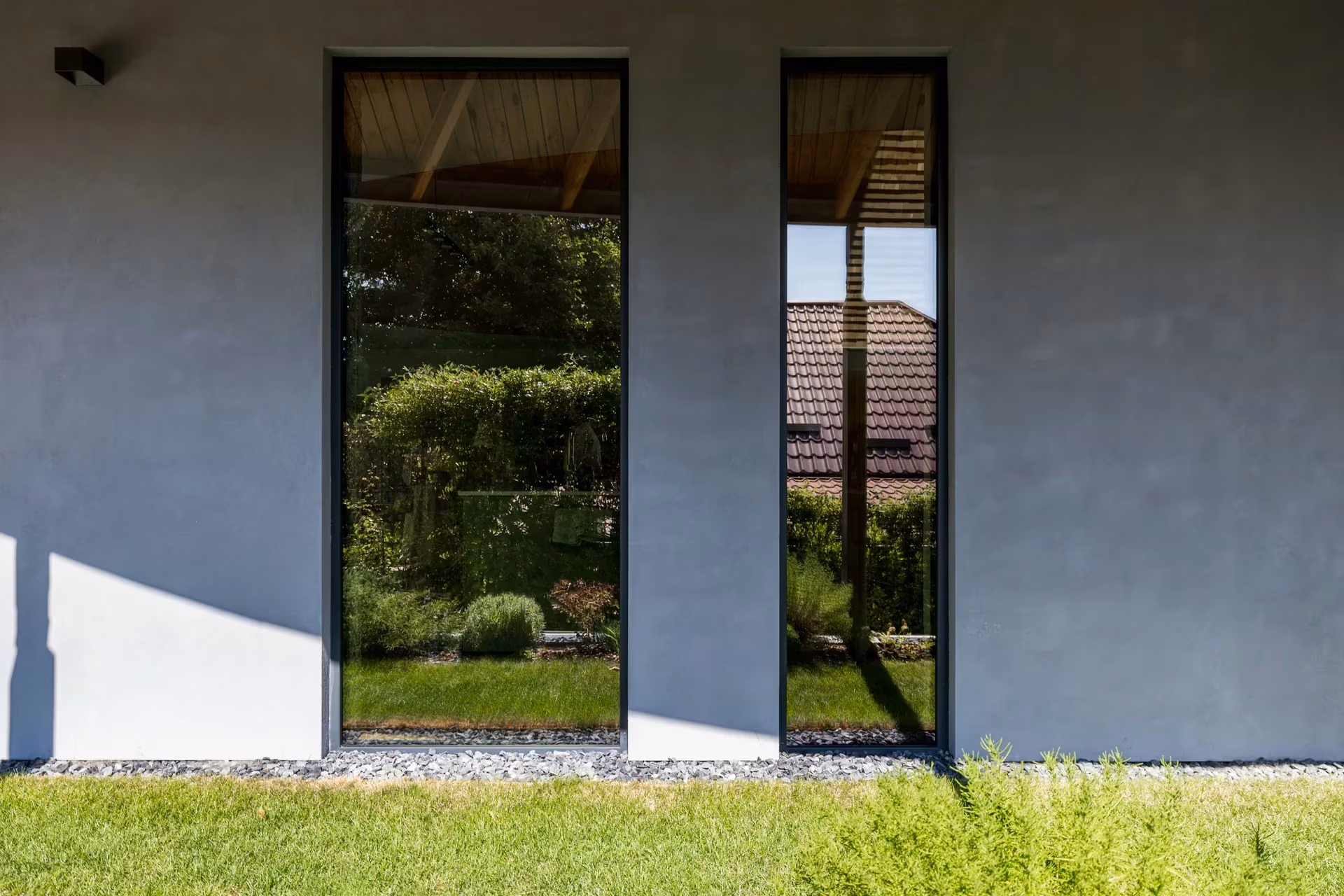 Two tall vertical windows on the house's grey façade, with a lawn in front.