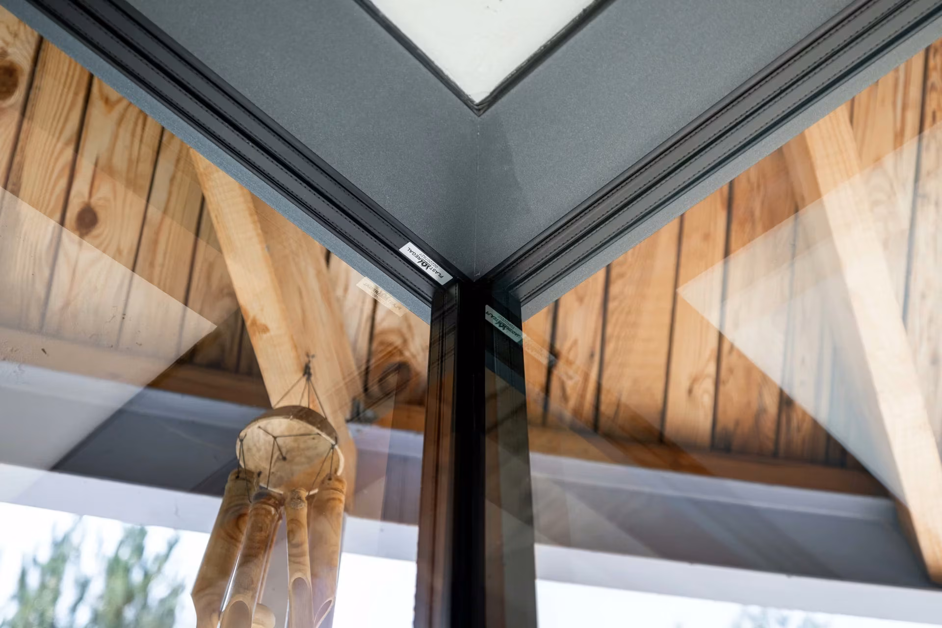 Upper junction of two glass panels with dark frames and a timber ceiling.