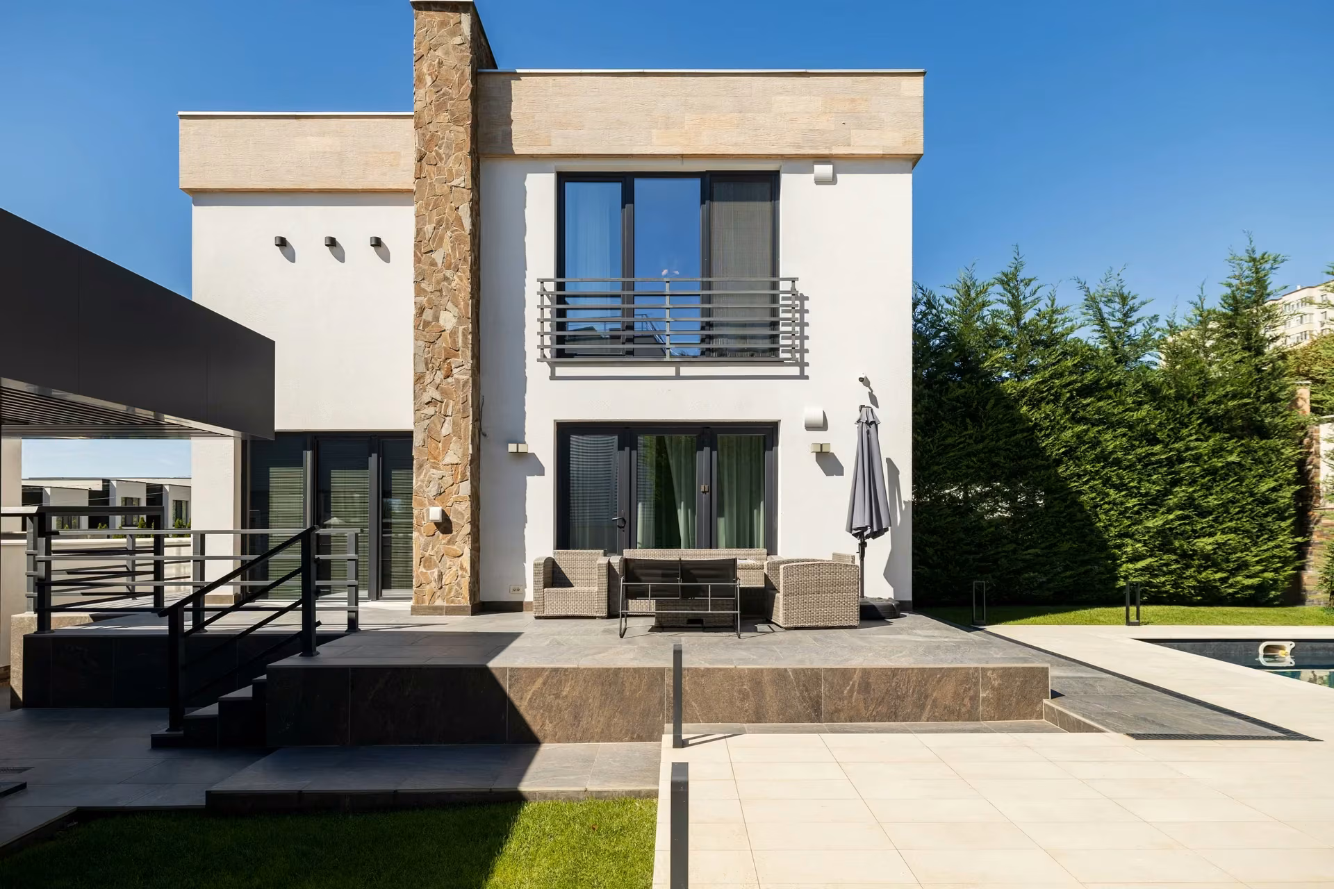 General view of a contemporary house with a white facade, stone-textured cladding and panoramic windows across two levels.