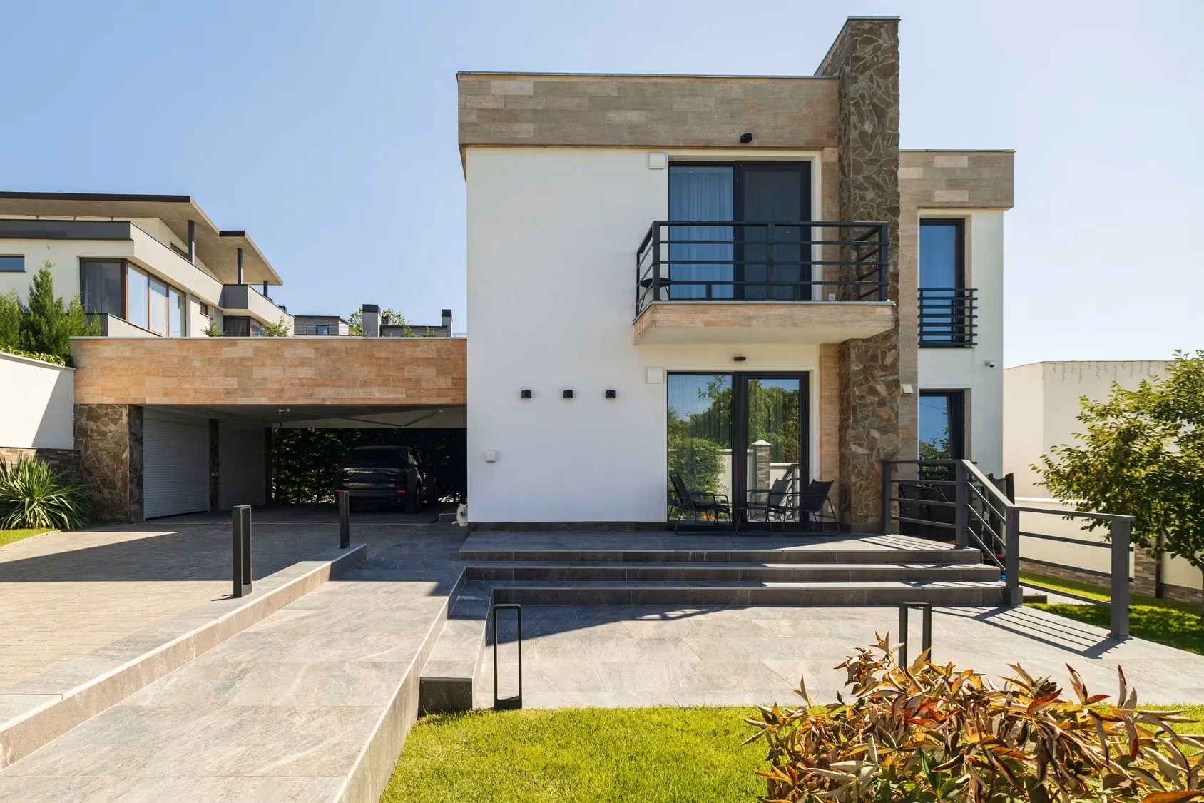 Contemporary facade viewed from the garden, with large windows, light-coloured walls and stone cladding.