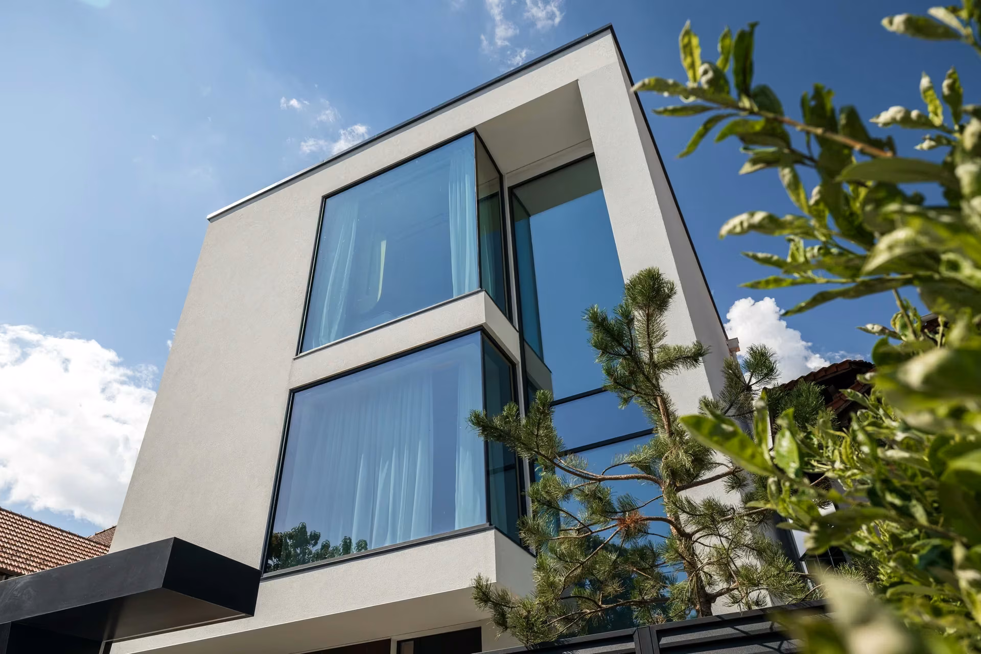 Fațada principală a unei case contemporane cu suprafețe vitrate panoramice, volume albe și profile închise la culoare.