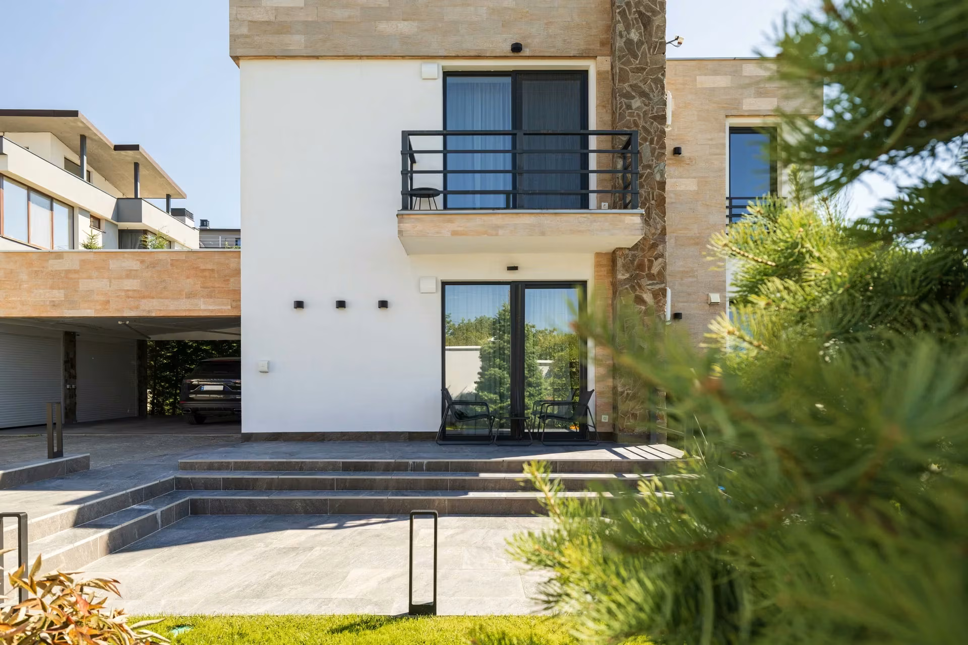 Contemporary house with a light-coloured façade, stone cladding and panoramic windows with dark frames.